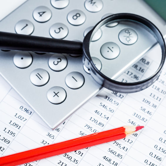 Image of a calculator, pencil and magnifying glass on a sheet of financial figures